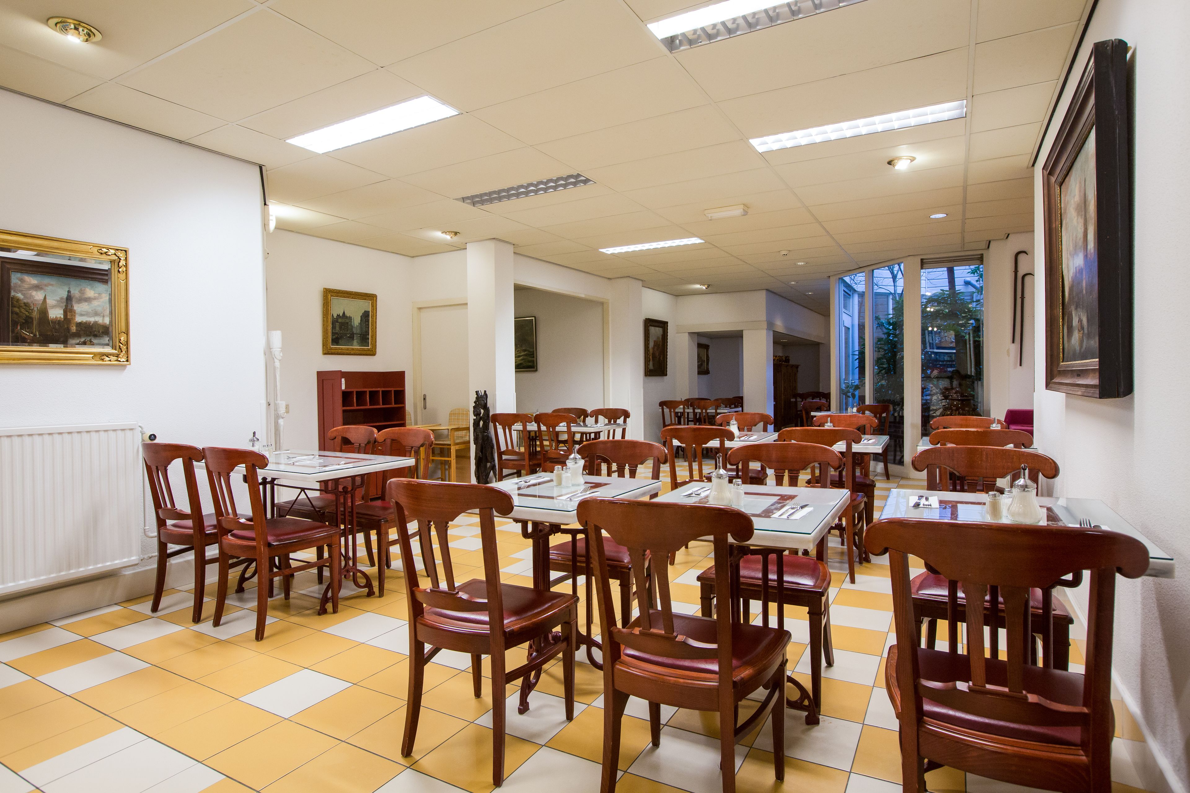 A dining area with wooden chairs and tables, white walls, and framed artwork.
