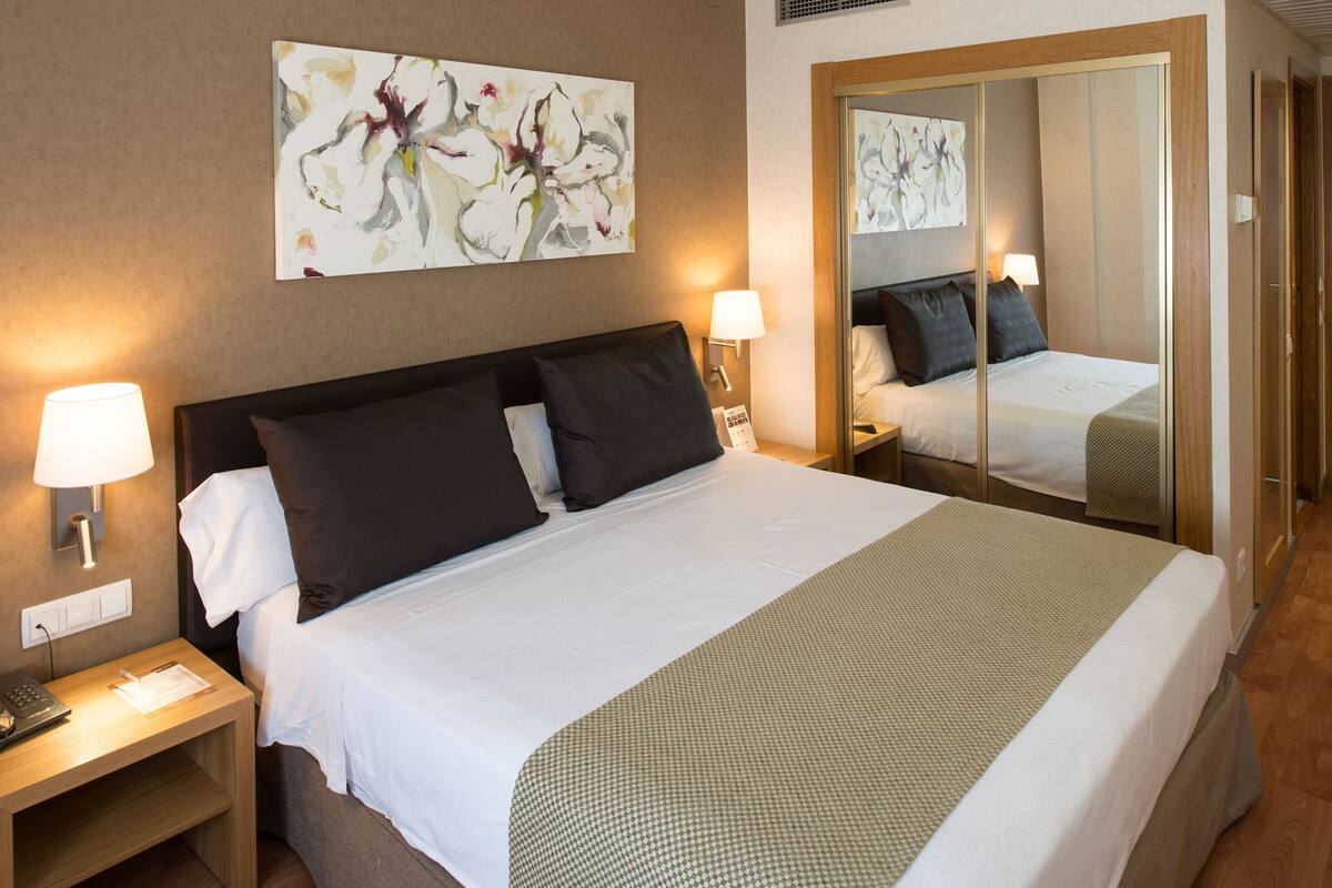 A hotel room with a bed, two bedside lamps, a nightstand, a telephone, and a mirror.
