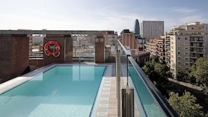 Una piscina en la azotea con vistas al paisaje urbano, incluyendo edificios modernos y un muro de ladrillo.