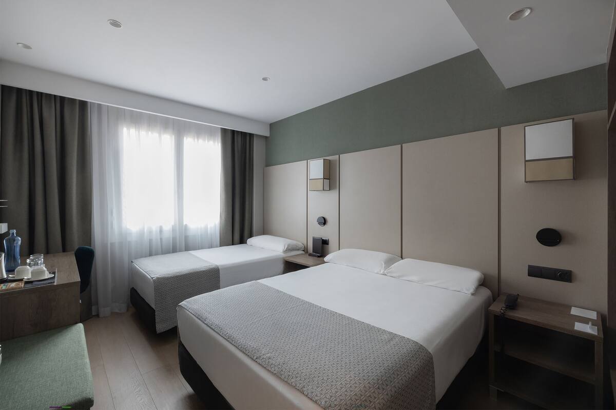 A hotel room with two beds, a desk, a chair, and a small table.