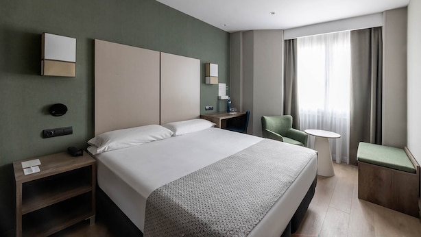 Una habitación de hotel moderna con una cama grande, un escritorio, una silla y una mesita.