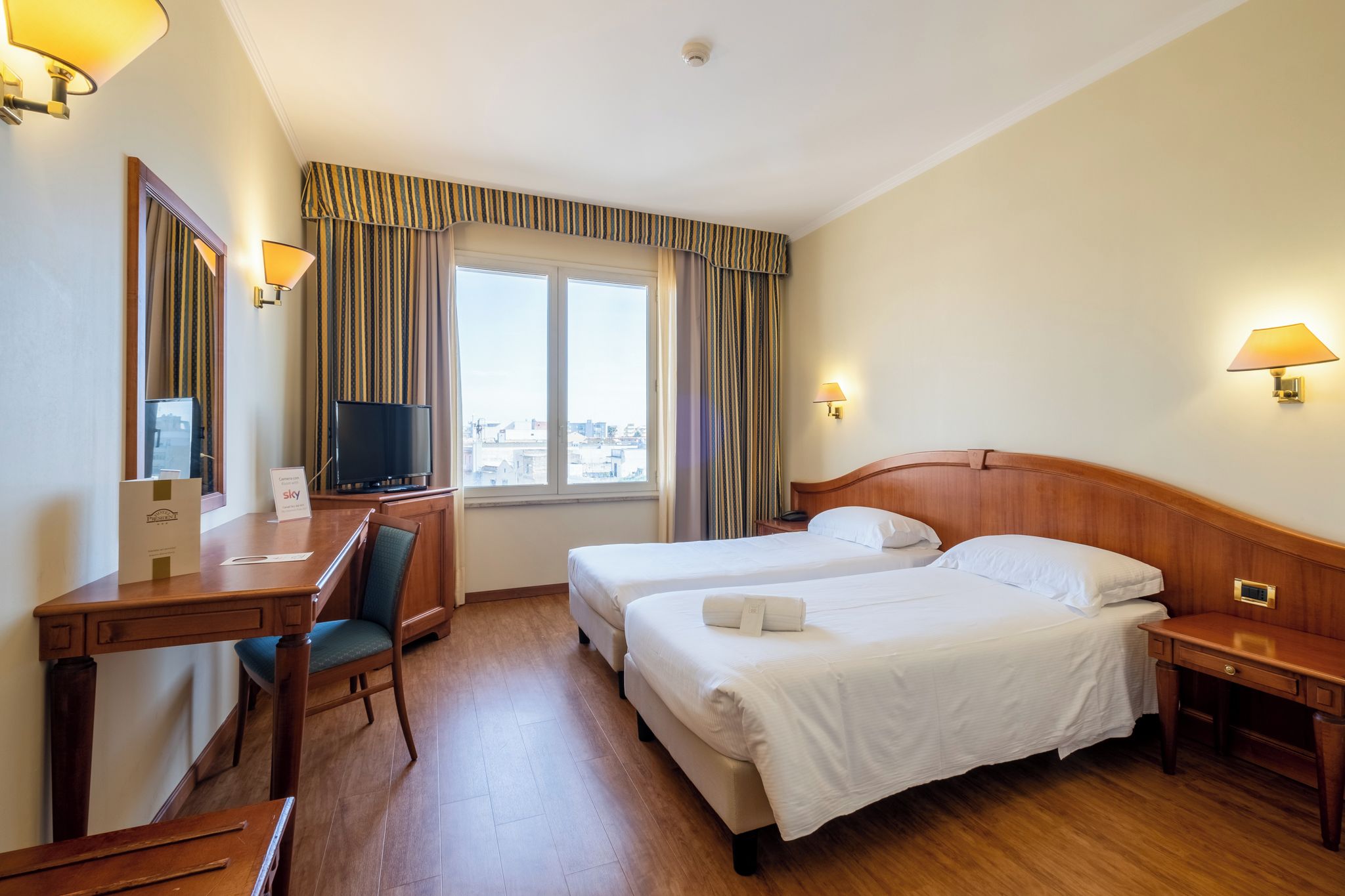 A hotel room with two beds, a desk, a chair, a television, and a window with curtains.