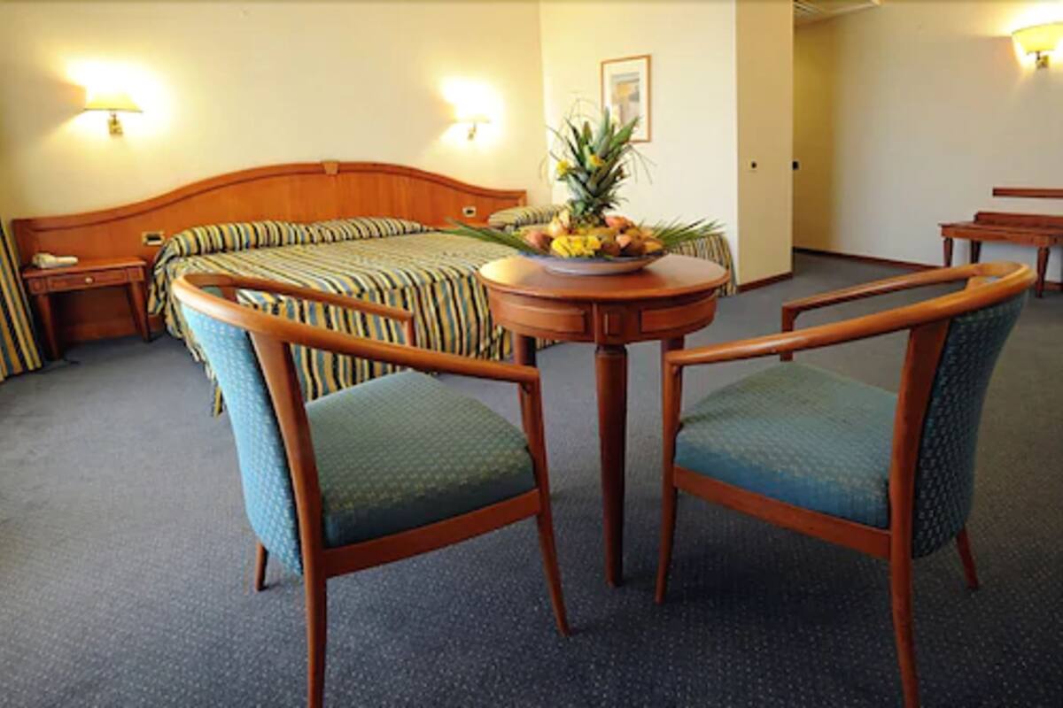 A hotel room with a bed, two armchairs, a small table with a fruit bowl, and a nightstand.