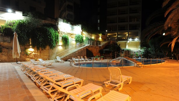 Un área junto a la piscina con sillas de descanso, una piscina pequeña y una escalera que conduce a un nivel superior.