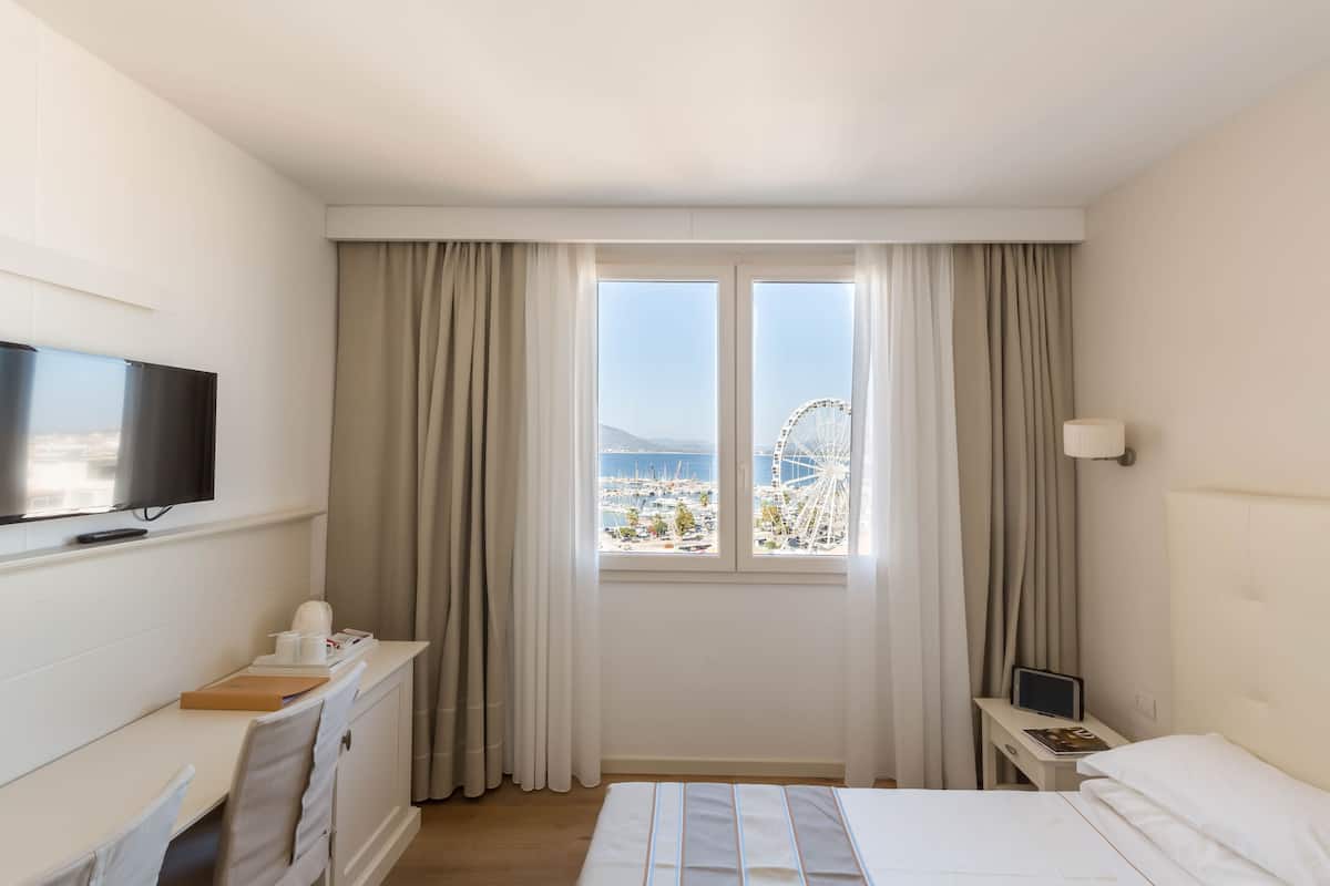 Una habitación de hotel con cama, escritorio, televisor y ventana con cortinas.