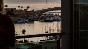 A sunset view from a balcony overlooking a marina with boats and buildings. - Hotel Catalunya (Alghero)