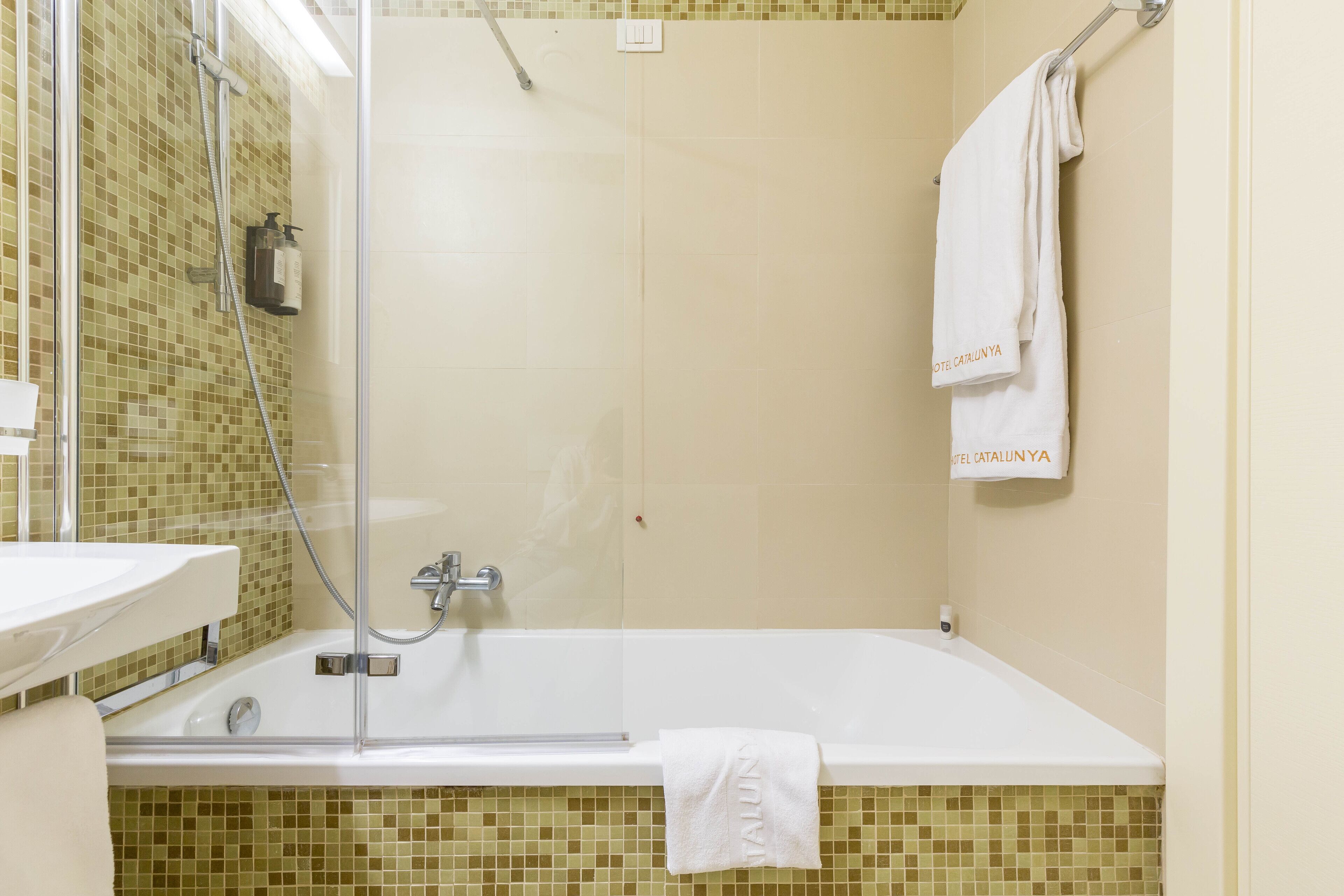 A bathroom with a glass-enclosed shower, a white bathtub, and a tiled wall.
