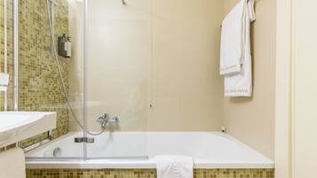 A bathroom with a glass-enclosed shower, a white bathtub, and a tiled wall.