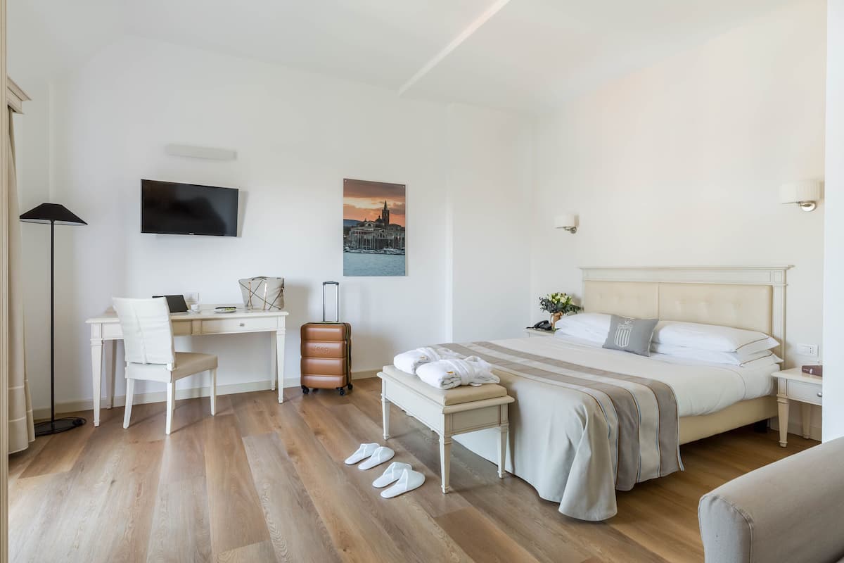 Habitación de hotel con cama, escritorio, silla, maleta y pantuflas en el suelo.