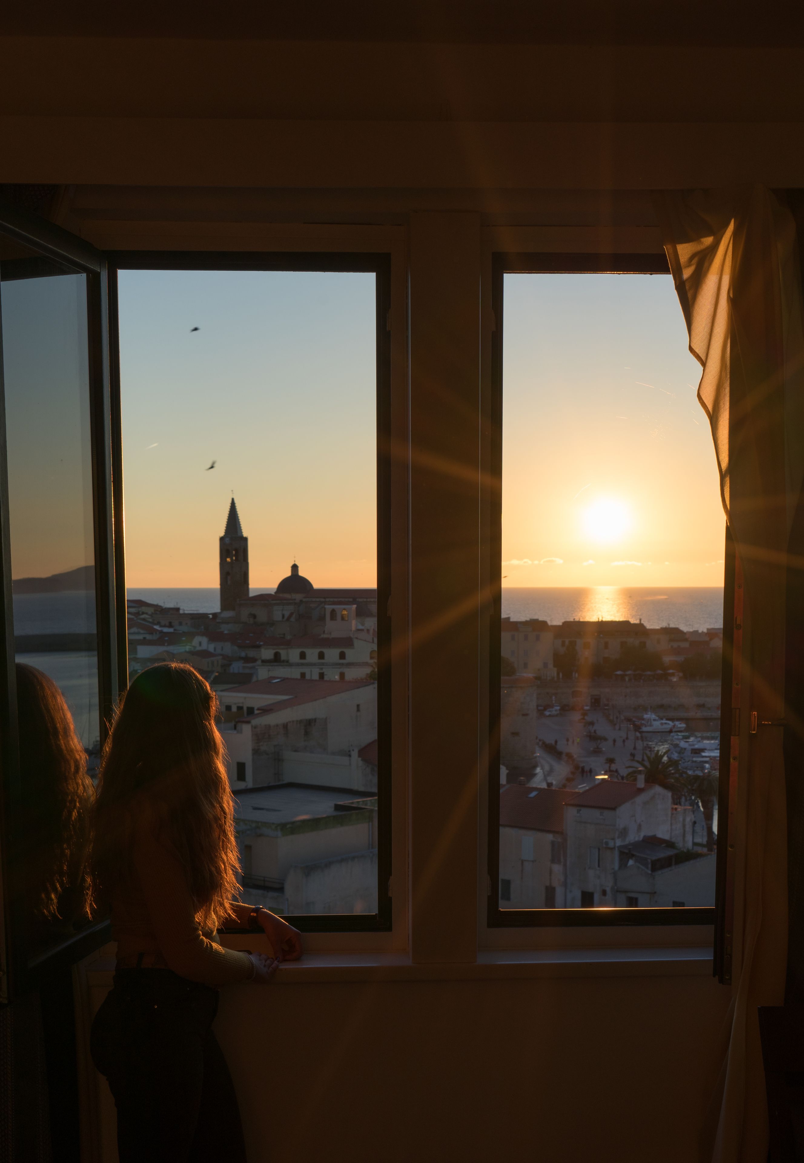 A room with a large window overlooking a cityscape at sunset, featuring a prominent tower and a body of water.