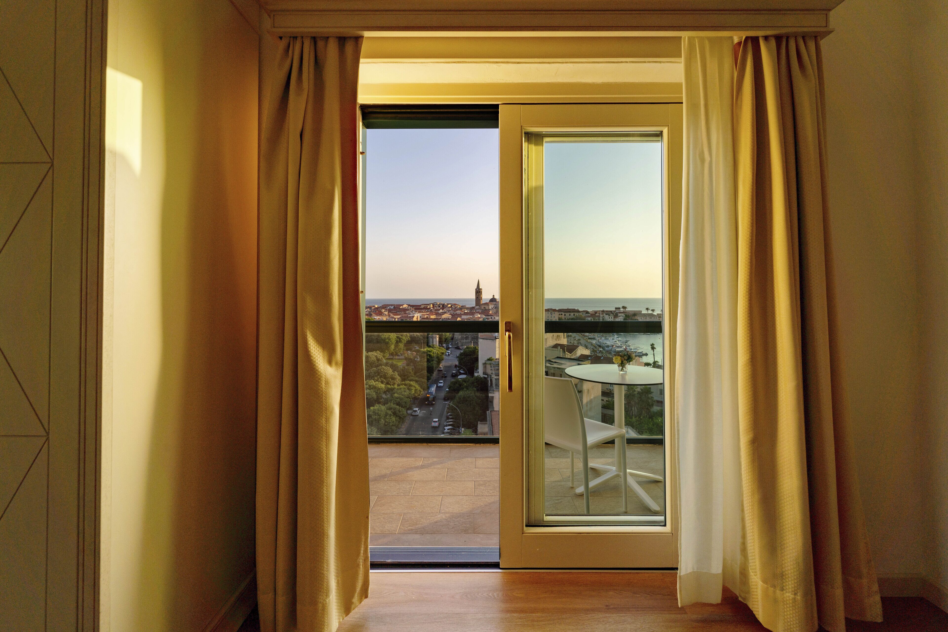Een kamer met een glazen schuifdeur die uitkomt op een balkon met uitzicht over de stad.