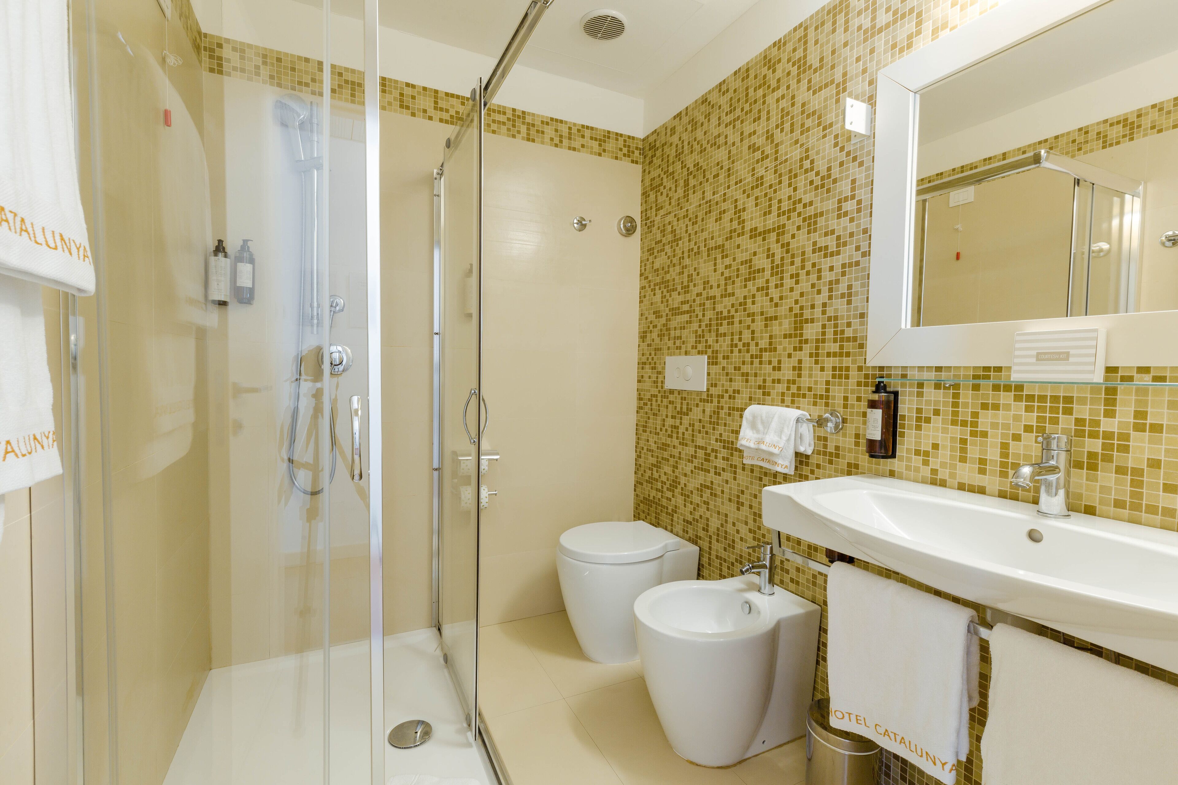 A modern bathroom with a glass-enclosed shower, two toilets, a bidet, and a sink with a mirror.