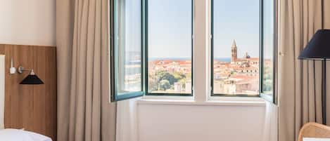 A hotel room with a bed, a chair, a lamp, and a window with a view of a cityscape.