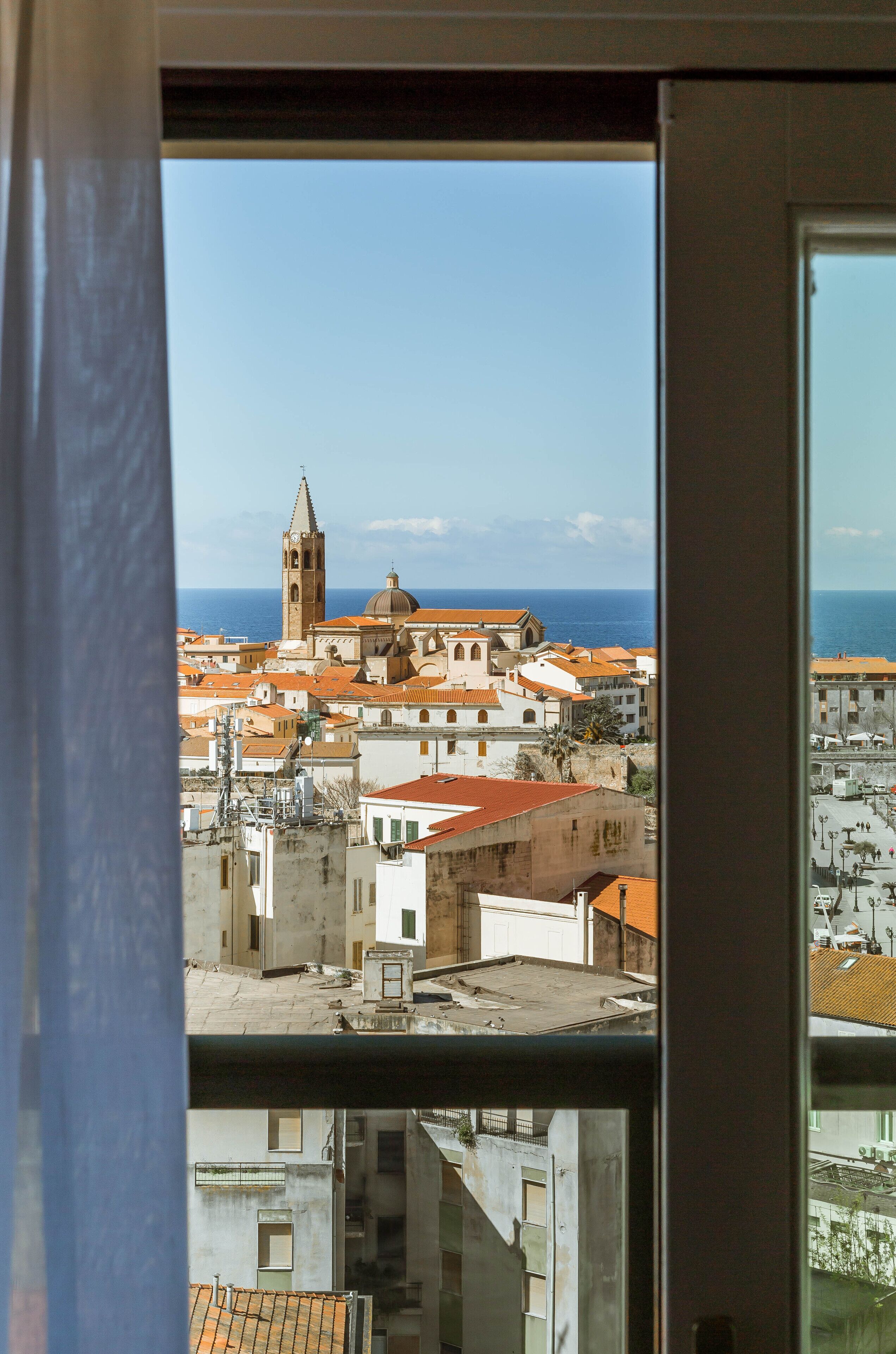 A coastal cityscape with a prominent tower and domed building, viewed through a window.