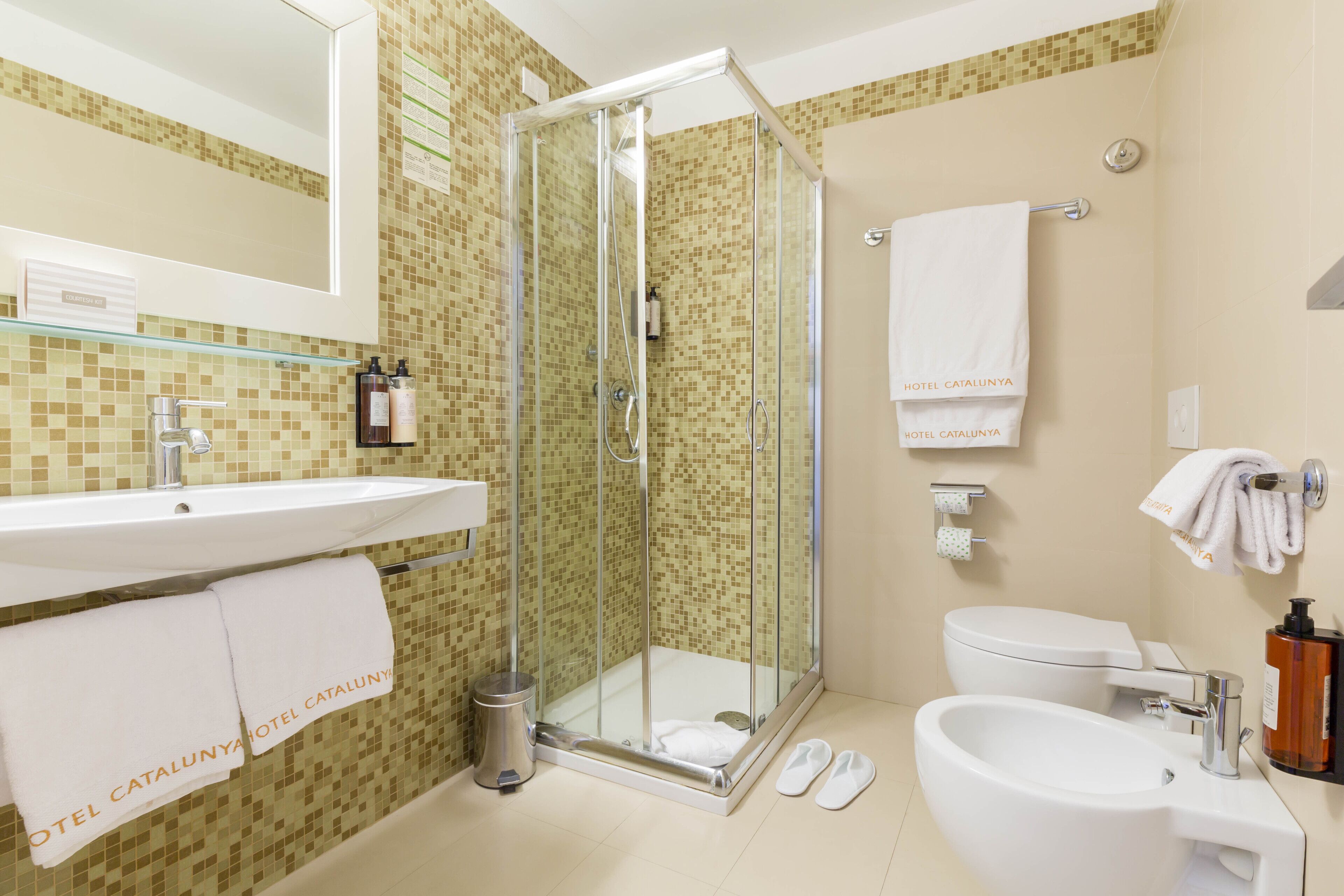 A modern bathroom with a glass-enclosed shower, a sink, a toilet, and a bidet.