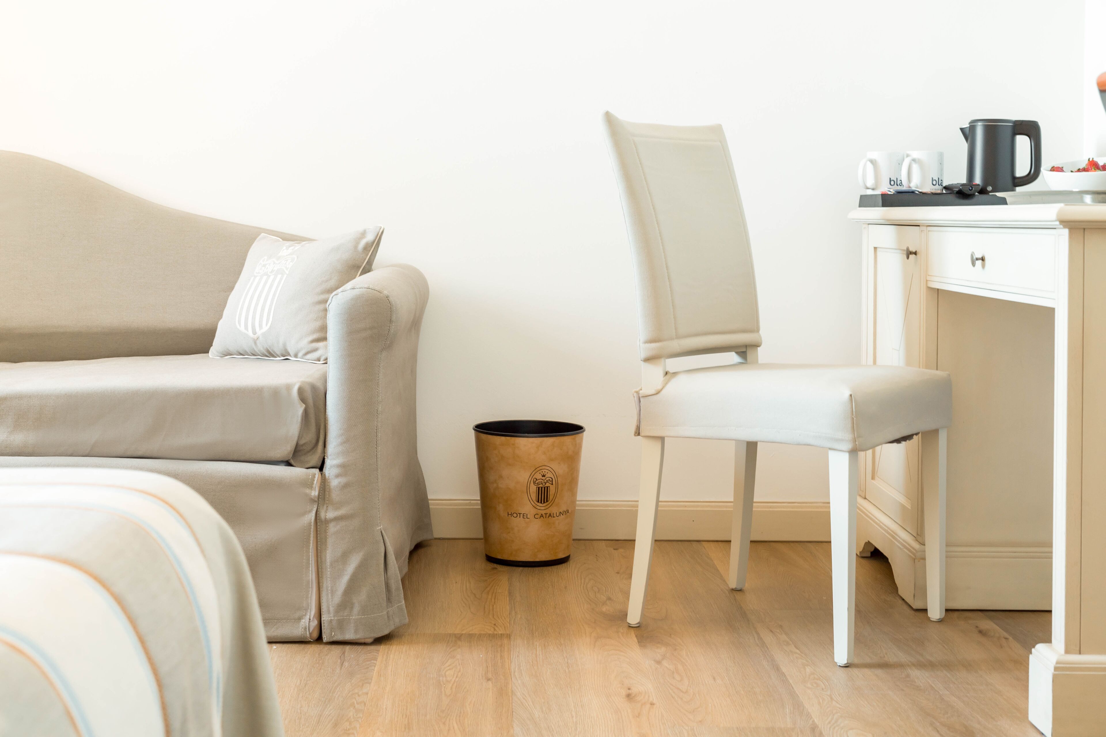 A hotel room with a sofa, a chair, a small trash bin, and a kitchenette area.
