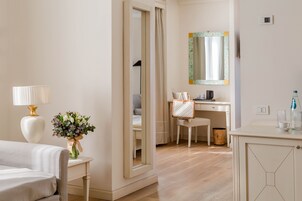 Una camera d'albergo con un letto, una scrivania, una sedia, uno specchio, una lampada e un vaso di fiori.
