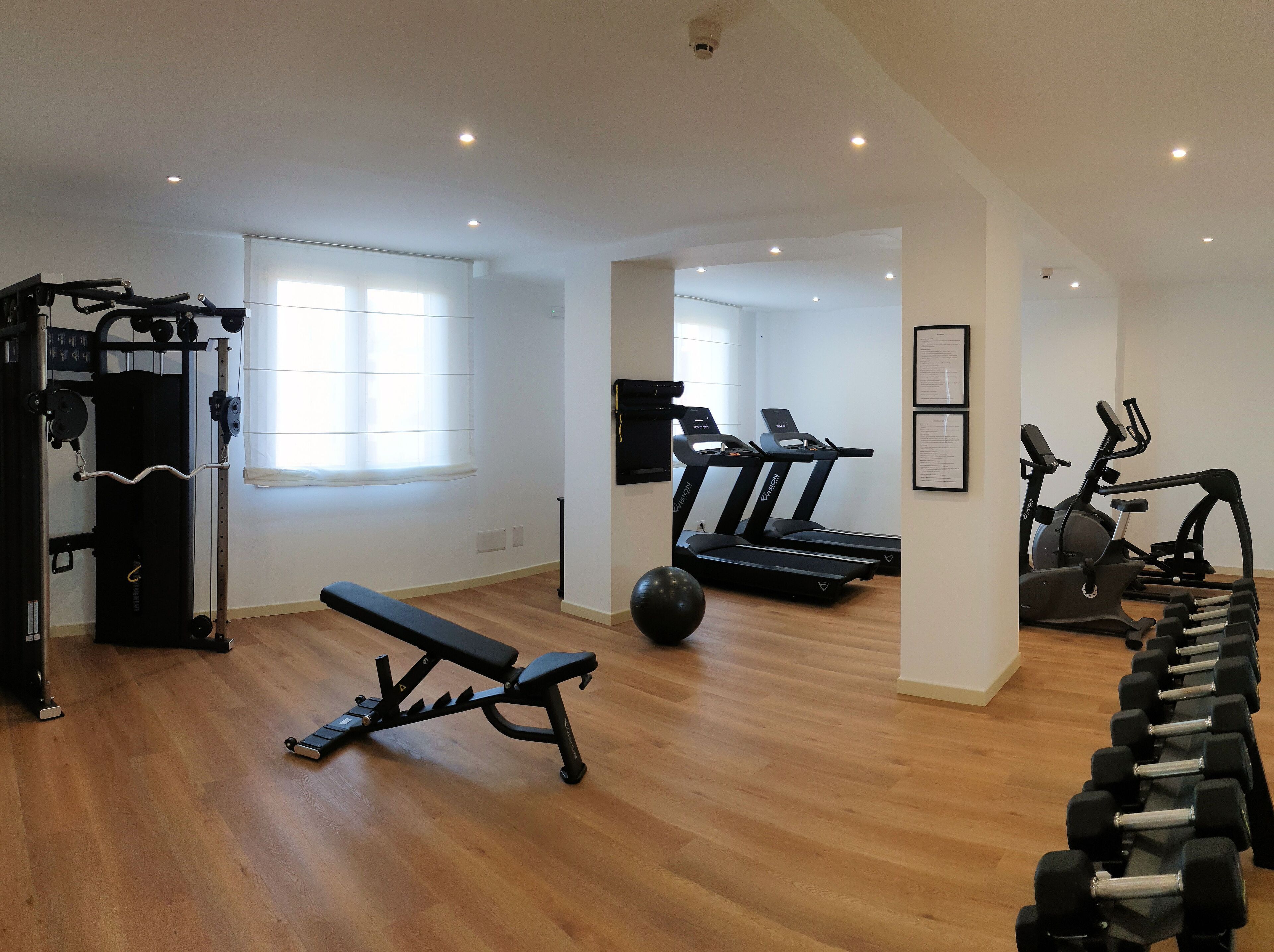 Une salle de sport équipée de matériel d’exercice, notamment des tapis de course, un banc et des haltères.