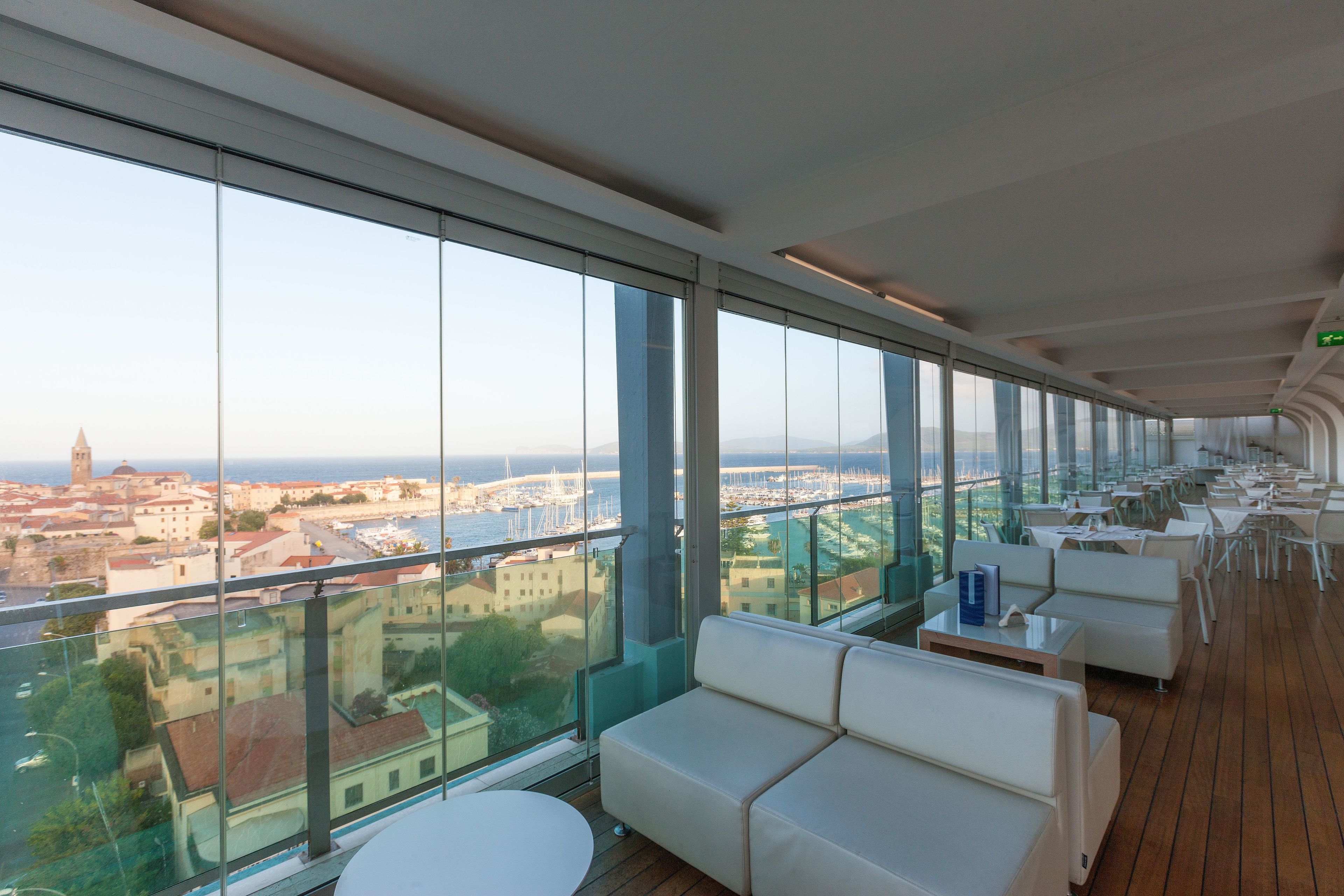 Un interior moderno con ventanas amplias que ofrecen vistas a la ciudad, un espacio de descanso con sofás blancos y suelo de madera.