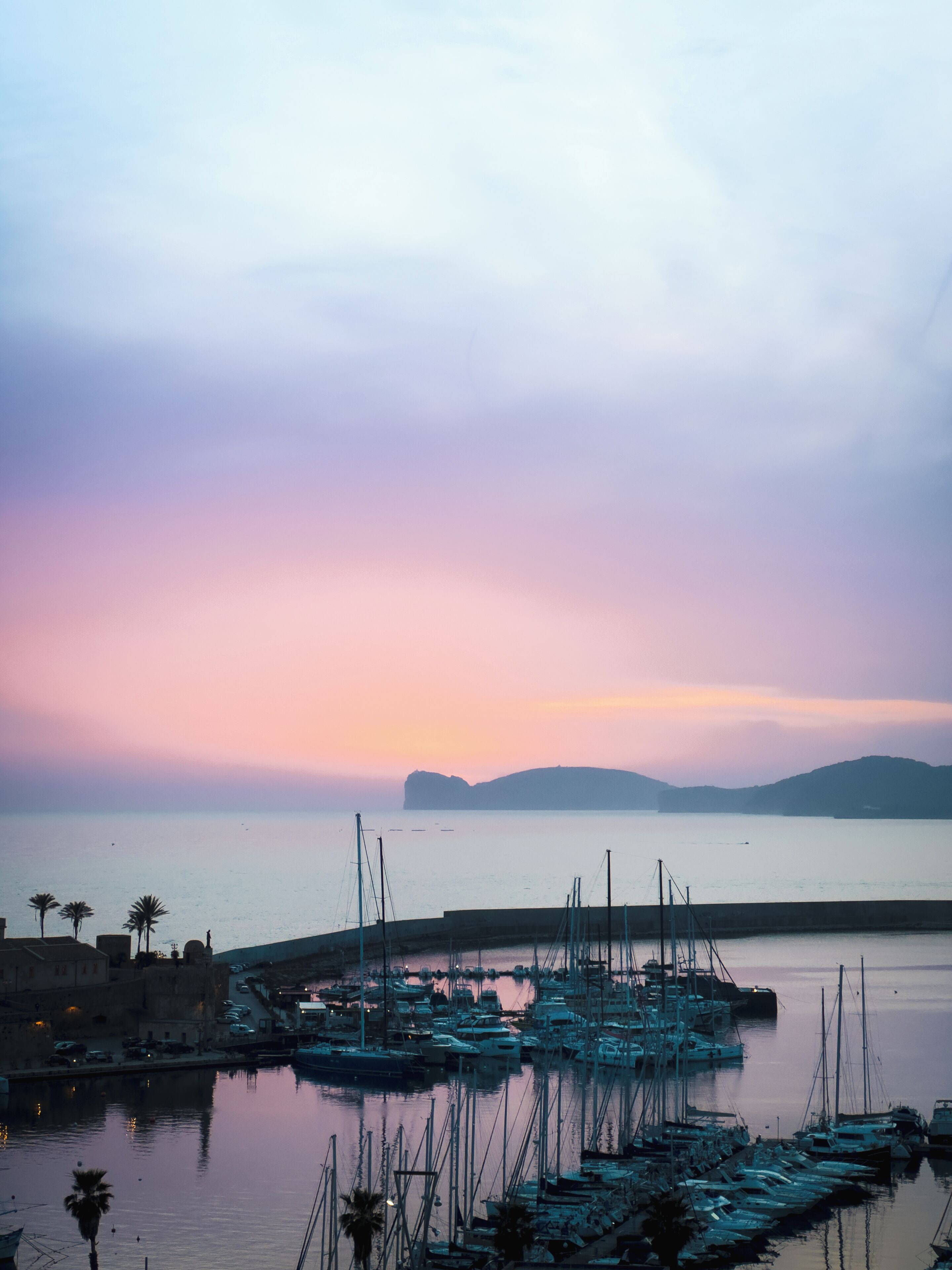Un port de plaisance avec des bateaux amarrés, une eau calme et une chaîne de montagnes à l’horizon.