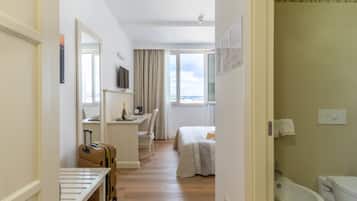 Une chambre d’hôtel comprenant un lit, un bureau, une chaise, une valise, un téléviseur et une salle de bain avec un bidet.