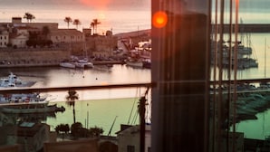 A sunset view from a balcony with a table and chairs, overlooking a marina with boats and buildings. - Hotel Catalunya (Alghero)