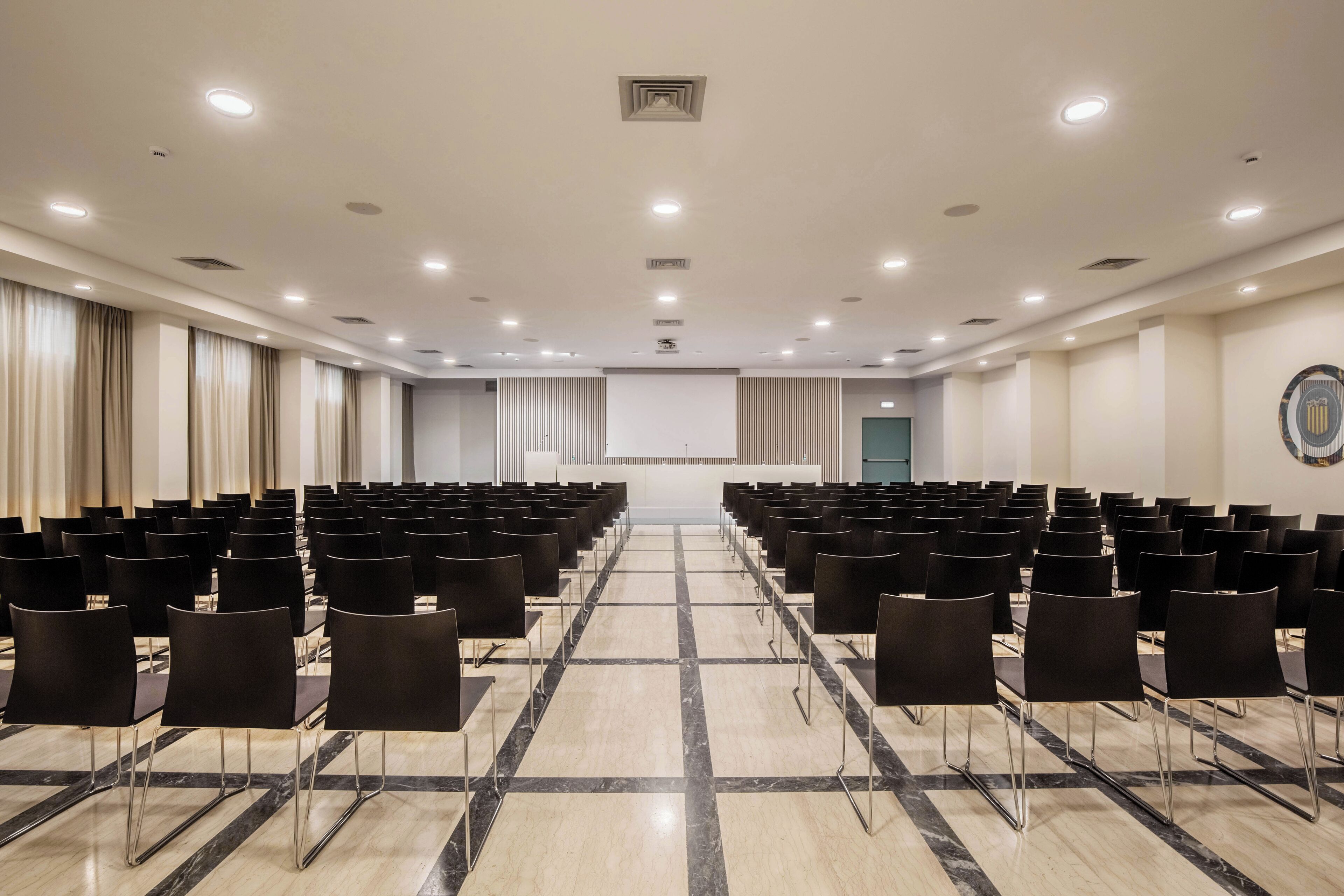 A conference room with rows of black chairs, a marble floor, and a stage at the front.