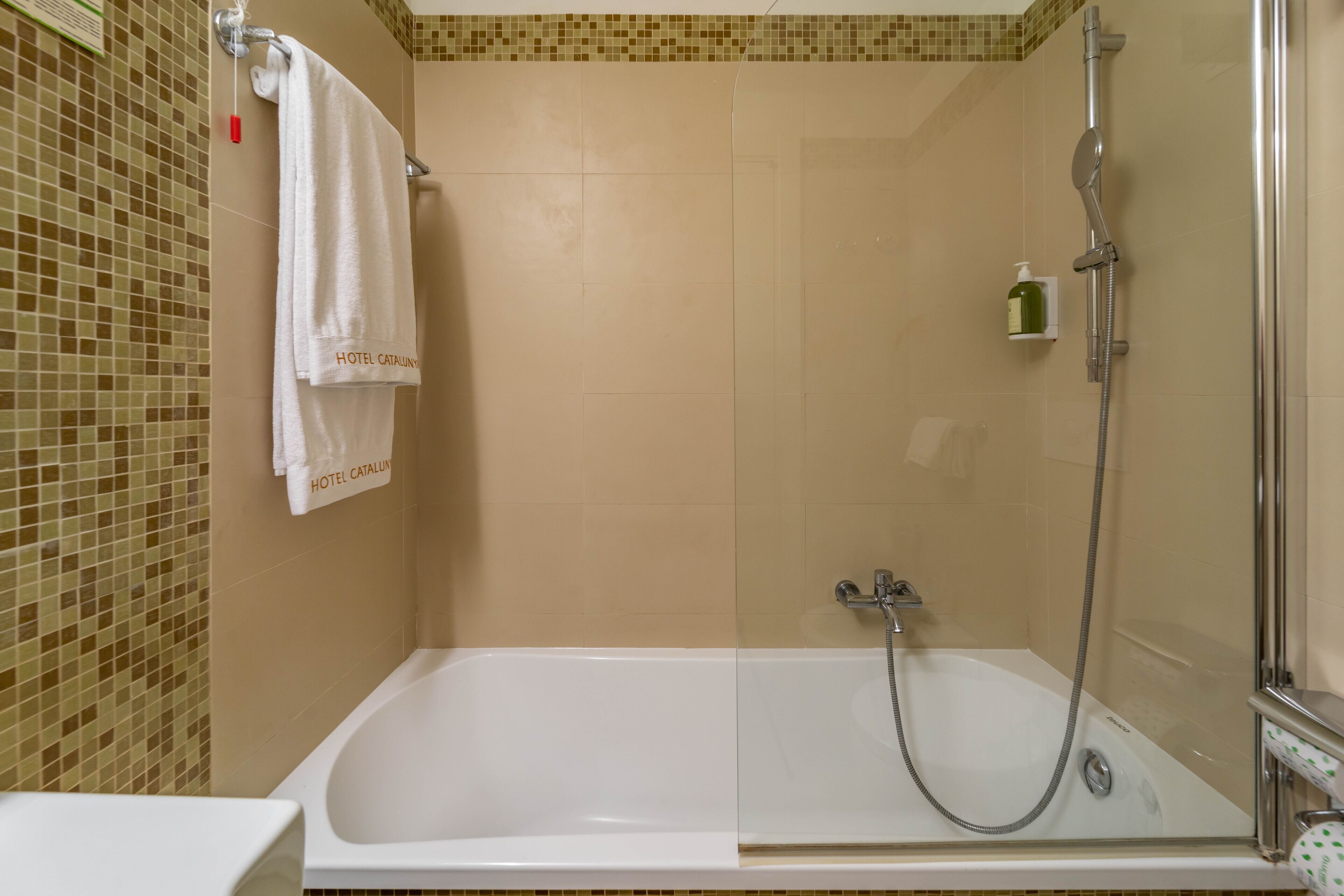 A bathroom with a glass-enclosed shower, a white bathtub, and a tiled wall with a mosaic pattern.