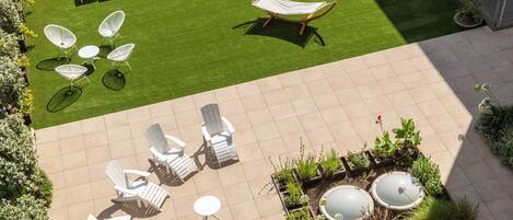 Una terraza en la azotea con sillones blancos, un rincón de descanso pequeño y un jardín con plantas en macetas.
