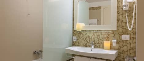 Een badkamer met een douchecabine van glas, een wastafel met spiegel erboven en een handdoekrek met handdoeken.