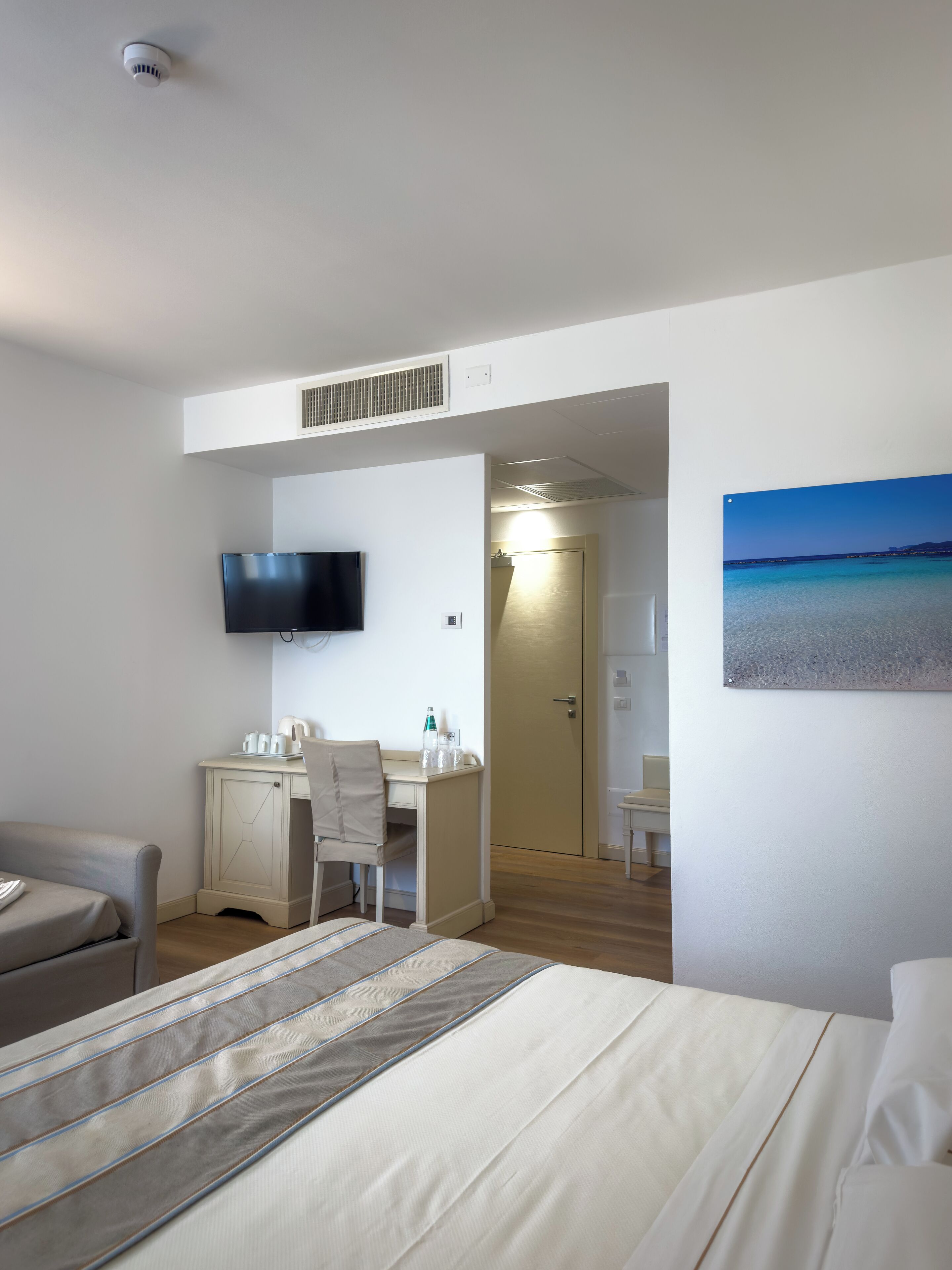 Una habitación de hotel con una cama, un escritorio, una silla, un televisor y una puerta que da a otra habitación.