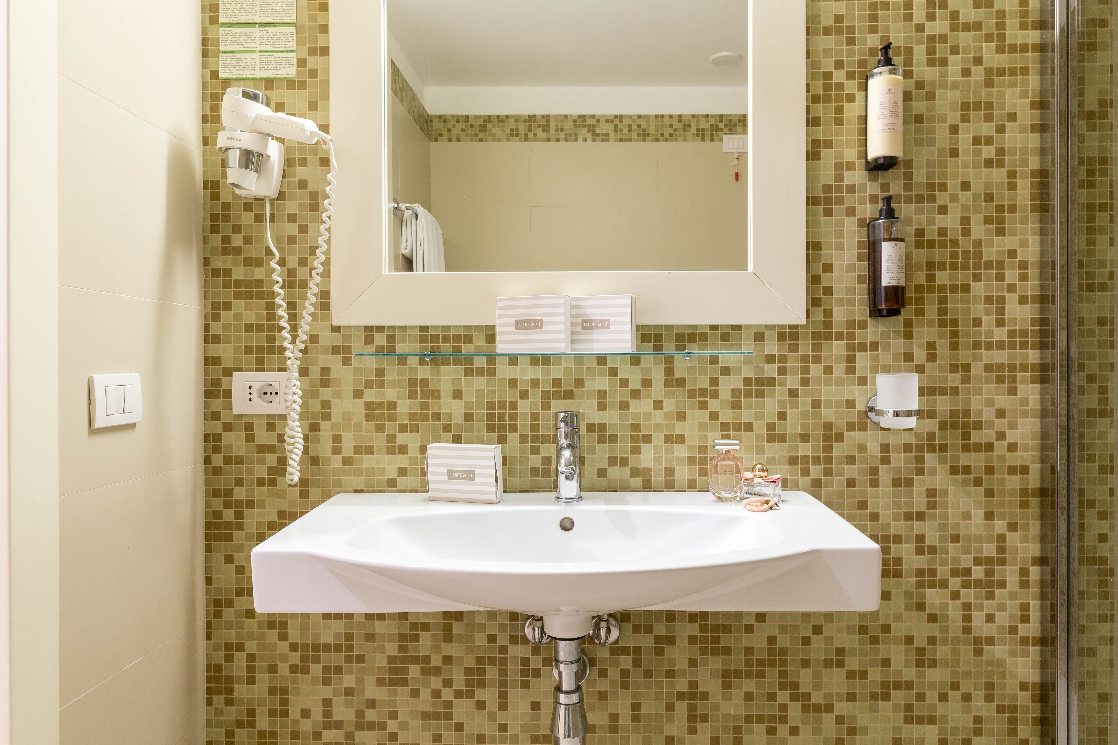 A bathroom with a white sink, a mirror, a hairdryer, and toiletries on the wall.