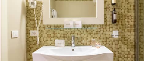 A bathroom with a white sink, a mirror, a hairdryer, and toiletries on the wall.