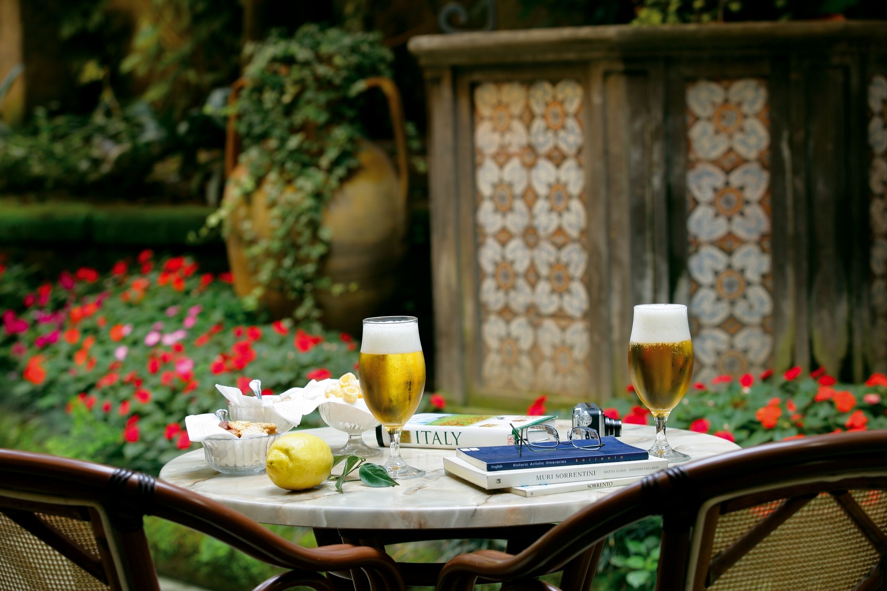 A table with two glasses of beer, a book titled "ITALY", a lemon, and a small bowl of snacks.