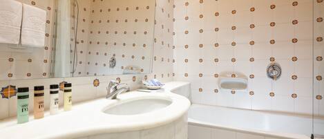 A bathroom with a large sink, a mirror, and a bathtub. There are toiletries on the sink counter.