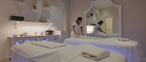 A spa room with two massage tables, a reception desk, and a large mirror.