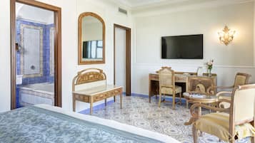 A hotel room with a bed, a desk with chairs, a television, and a bathroom with a bathtub and mirror.