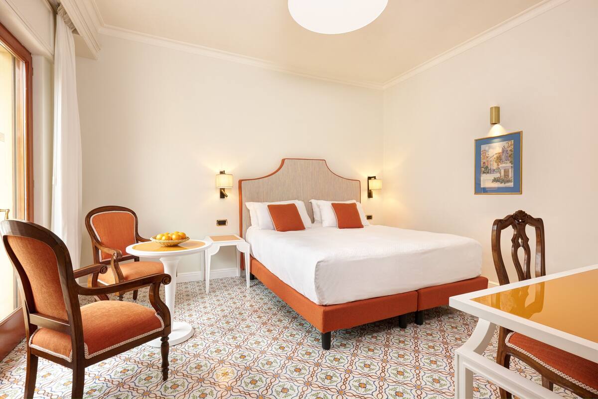A hotel room with a bed, two chairs, a small table, and a painting on the wall.