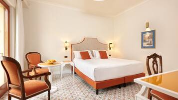 A hotel room with a bed, two chairs, a small table, and a painting on the wall.