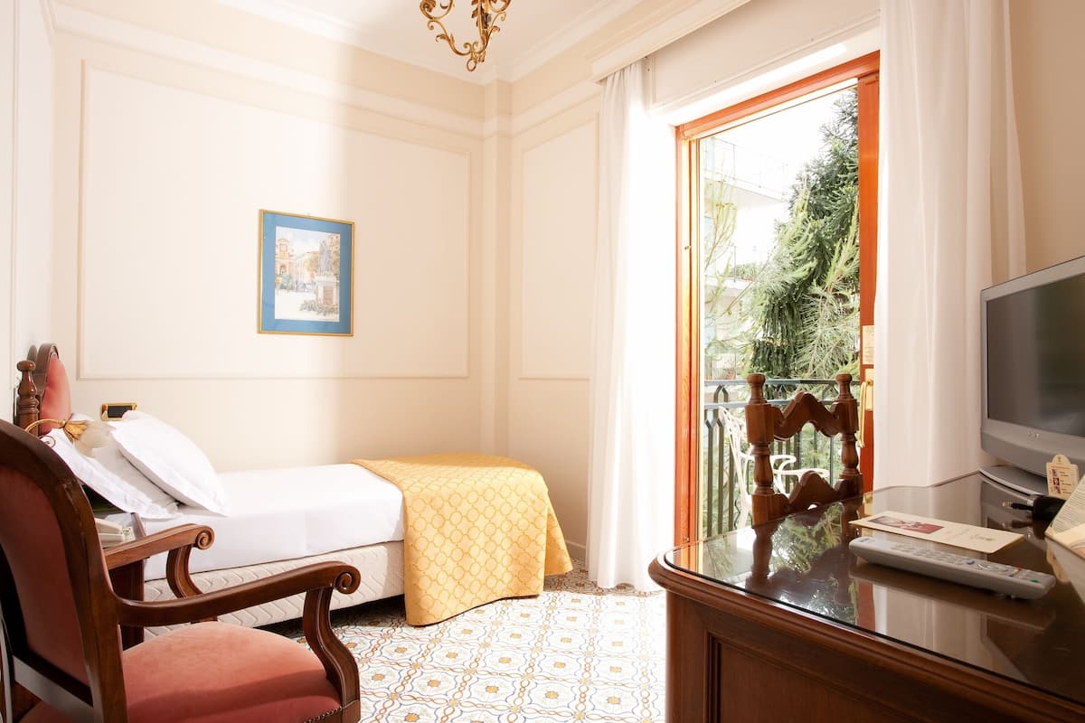 A hotel room with a bed, a chair, a television, and a window with a view of greenery.