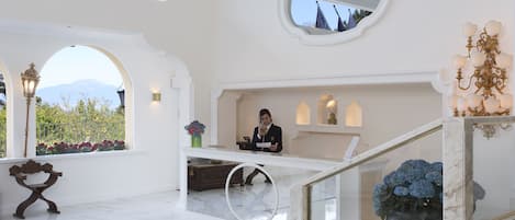 A spacious lobby with a marble floor, a reception desk, and a view of mountains through large windows.