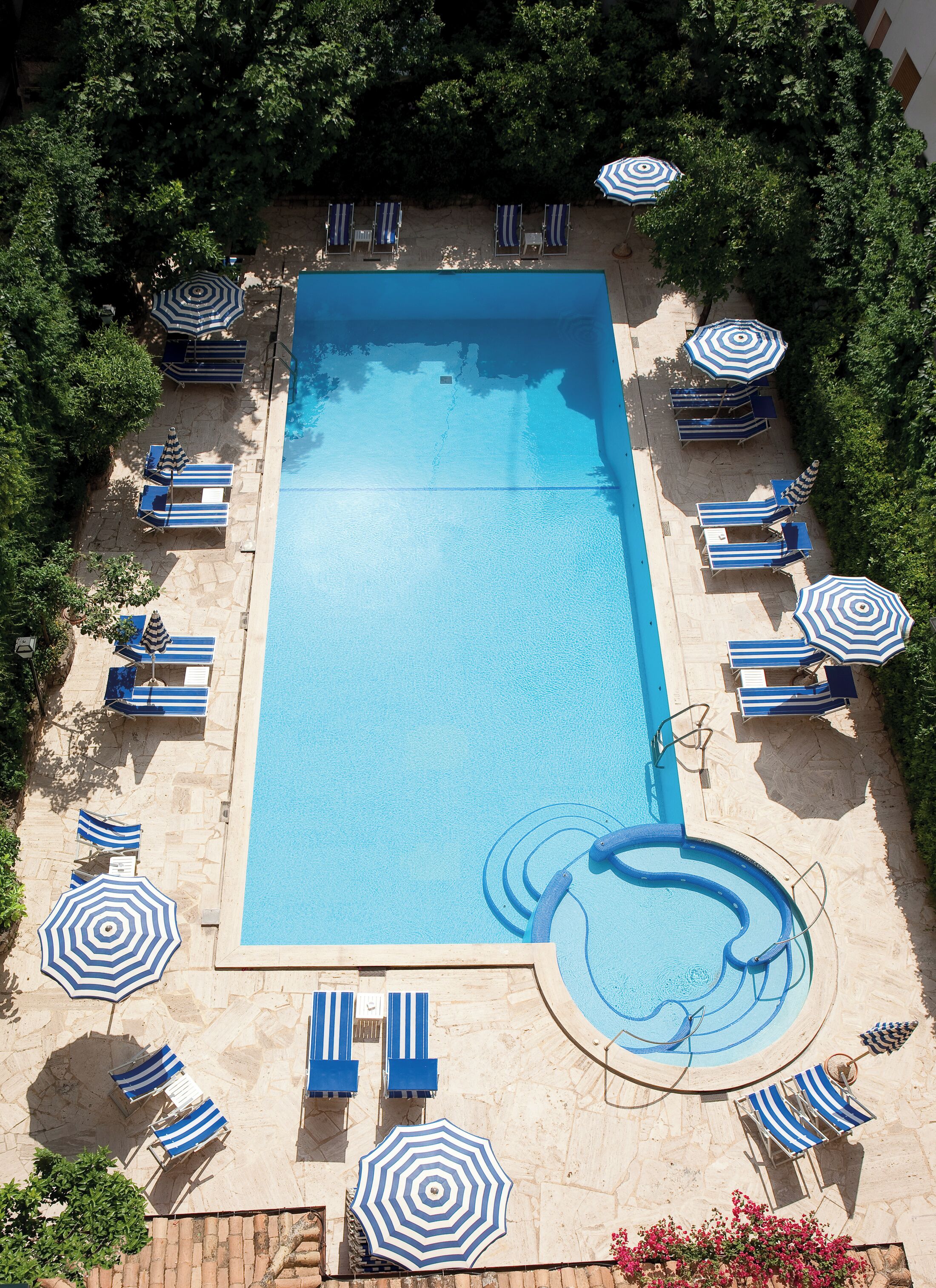 A rectangular swimming pool with blue and white striped lounge chairs and umbrellas arranged around it.