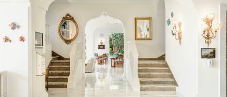 A grand hallway with marble flooring, a staircase, and a dining area with a view of greenery.
