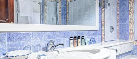 A bathroom with a large mirror, a sink, and a shower. There are toiletries on the sink counter.