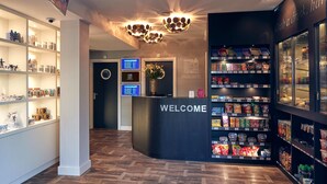 A hotel reception area with a 'WELCOME' sign, a digital screen, and shelves stocked with snacks and beverages. - Singel Hotel Amsterdam (Amsterdam)