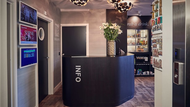 A reception desk with 'INFO' signage, a digital display, and a floral arrangement. - Singel Hotel Amsterdam (Amsterdam)
