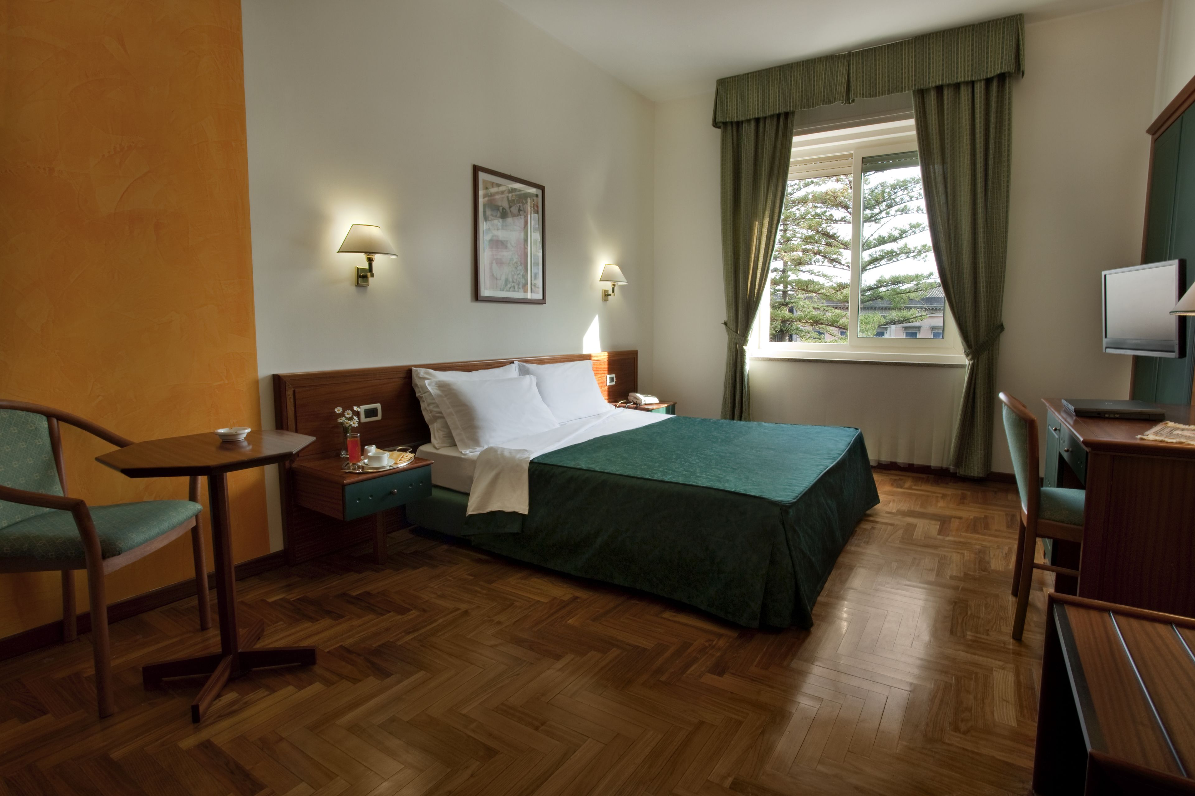 Une chambre d’hôtel comprenant un lit, une table de chevet, une lampe, une chaise, un bureau et un téléviseur.