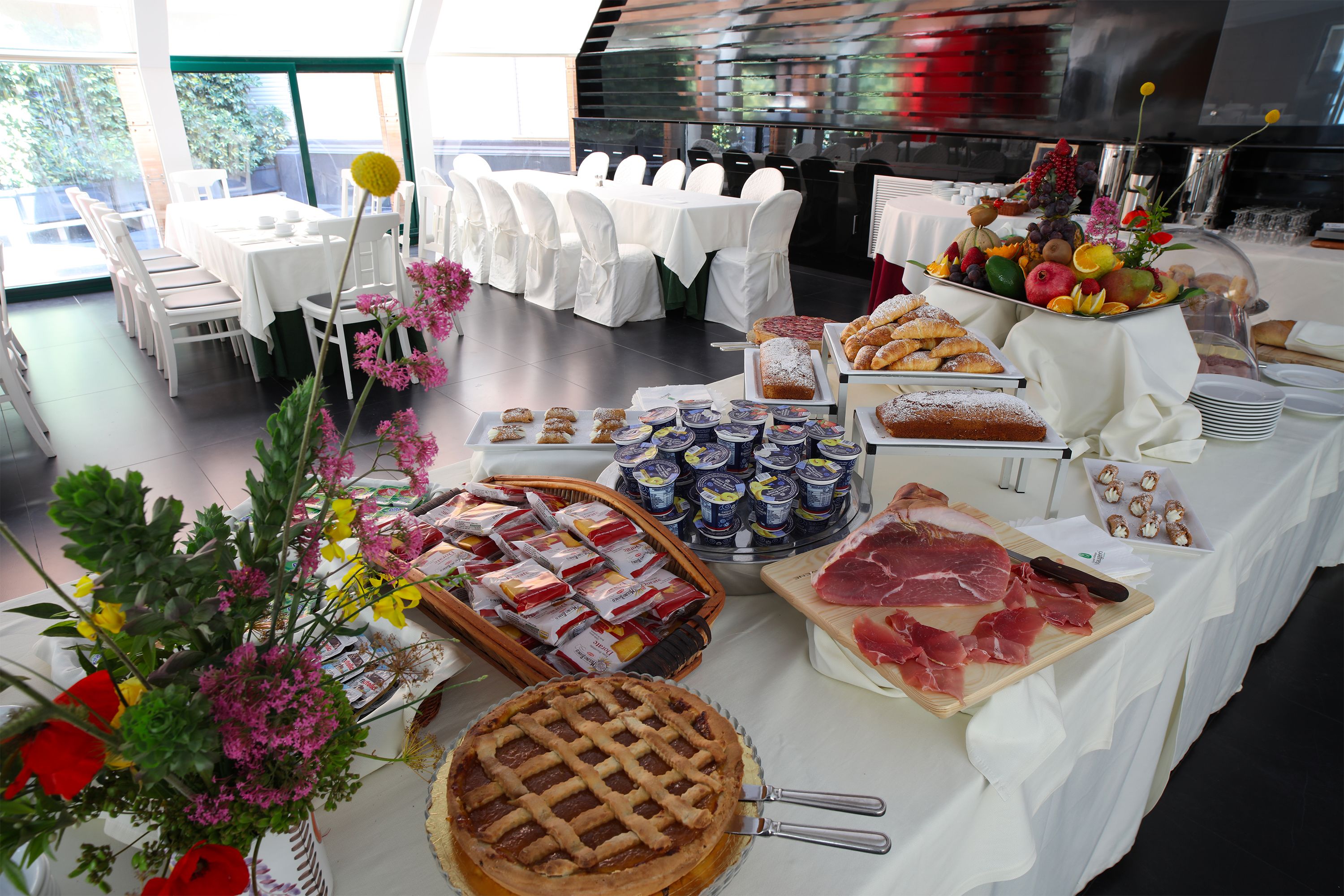 A buffet setup with various food items, including pastries, meats, and fruits, arranged on tables covered with white tablecloths.