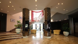 A spacious lobby with a marble floor, a staircase with red accents, and potted plants. - Grande Albergo Maugeri (Acireale)