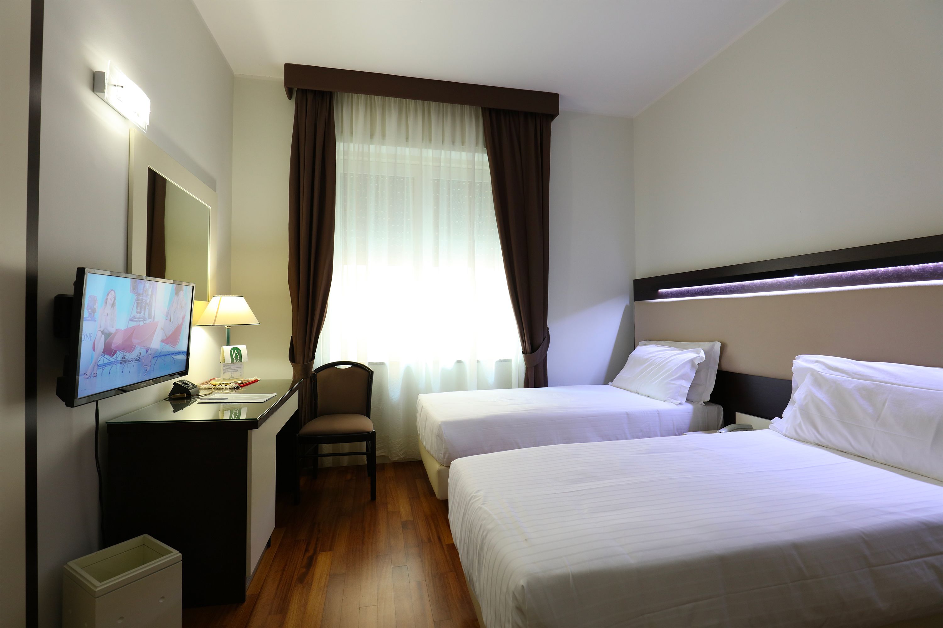 A hotel room with two beds, a desk with a TV, a chair, and a window with curtains.